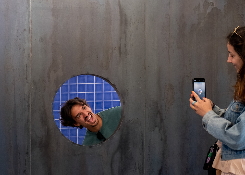 um visitante pos a cabeça no boraco da parede enquanto outra visitante tira forografia