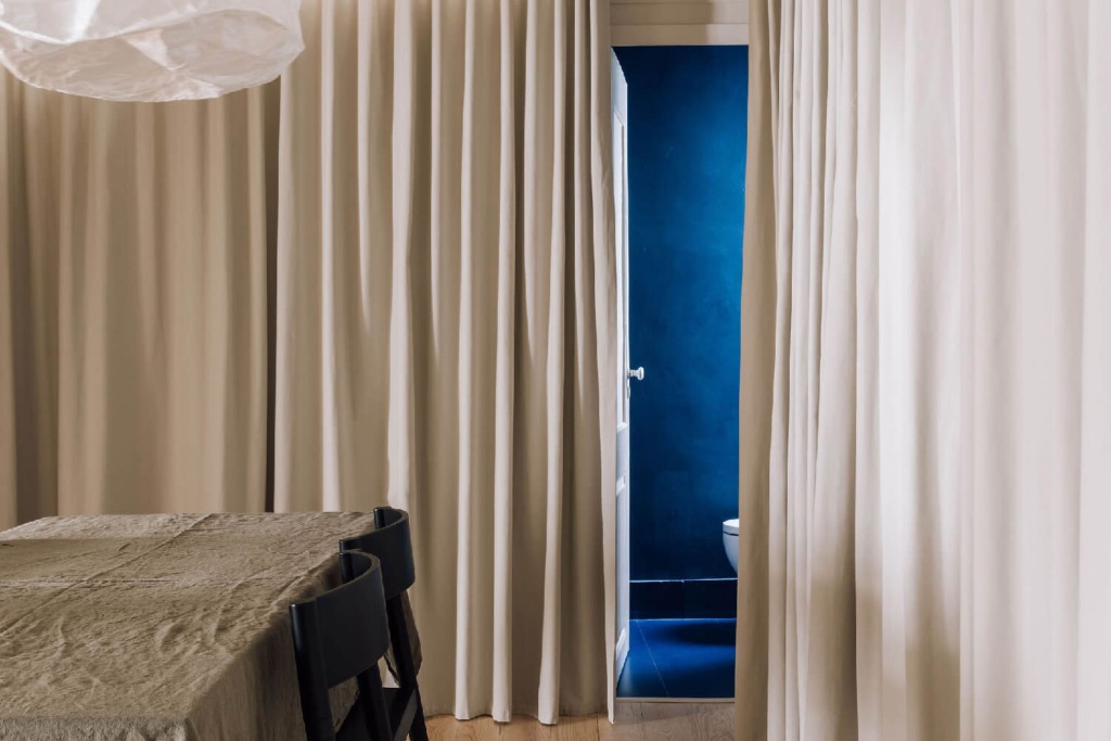 interior de apartamento dividido por cortina em que se deixa ver a parede azulão da casa de banho